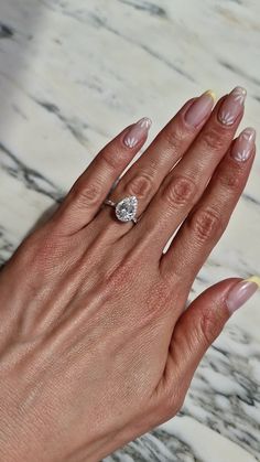 a woman's hand holding a diamond ring on top of her left hand, with marble background