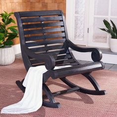 a wooden rocking chair with a white towel on it's arm and potted plant in the background