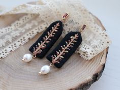 two black earrings with gold leaves and pearls on top of a piece of wood next to a lace doily