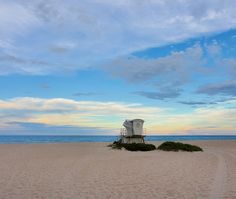 a lifeguard chair sitting on top of a sandy beach next to the ocean at sunset