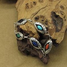 This vintage sterling silver bracelet is a stunning piece of jewelry that showcases intricate craftsmanship. The bracelet features a malachite, lapis lazuli, coral, turquoise, and onyx stones bezel set in a shadow box design. The bracelet measures 8 1/8" end to end. The stones measure 10.5mm wide and 5.5mm tall. The shadow boxes measure 1 3/8" wide including the bails and just over 1/2" tall. The artist's hallmark (J) is stamped on the back of the malachite shadow box. (STERLING) is also stamped Southwestern Silver Bracelets With Natural Stones, Multicolor Inlay Sterling Silver Bracelets, Multicolor Sterling Silver Bracelet With Inlay, Multicolor Sterling Silver Bracelets With Inlay, Artisan Sterling Silver Bracelet With Inlay, Southwestern Multi-stone Bracelet Jewelry, Southwestern Silver Multi-stone Bracelets, Southwestern Silver Bracelet With Multi-stone, Collectible Silver Bracelets With Natural Stones