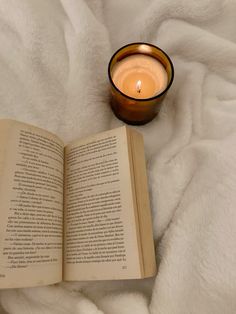 an open book next to a candle on a white blanket