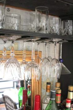 many wine glasses are lined up on the shelf in front of some bottles and glasses