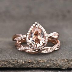 an engagement ring set with a pear shaped morganite surrounded by diamonds on top of a stone slab