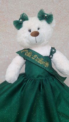 a white teddy bear wearing a green dress with gold lettering on it's chest