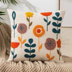 a white pillow with orange, blue and green flowers on it sitting on a couch