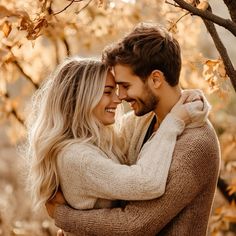 a man and woman embracing each other in front of a tree with leaves on it