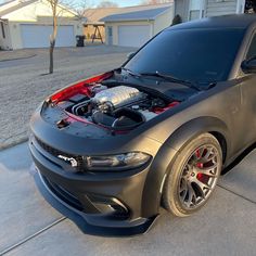 the car is parked on the driveway with it's hood up and engine bay open