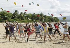 a group of people standing on top of a sandy beach next to the ocean holding frisbees