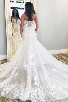 a woman standing in front of a mirror wearing a wedding dress