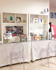 two clear chairs are sitting in front of a table with many items on it and bookshelves behind them