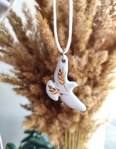 a ceramic bird ornament hanging from a white cord on a plant in front of a window