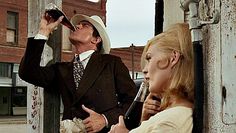 a man and woman standing next to each other in front of a telephone pole talking on cell phones