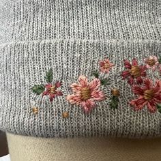 a knitted hat with flowers on the front and side, sitting on a mannequin's head