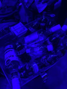 an assortment of beer bottles and cans in a plastic container on a table with blue lighting