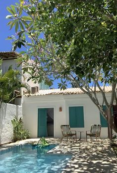 an outdoor swimming pool next to a white house with blue shutters and green doors