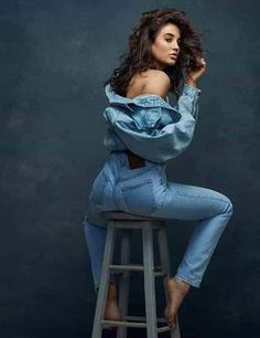 a woman sitting on top of a wooden stool wearing blue jeans and a hoodie