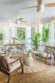 a porch with wooden furniture and plants on the floor, in front of large windows