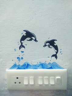 two dolphins jumping out of the water on top of a light switch cover in front of a white wall