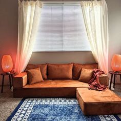 a living room with a couch, ottoman and two lamps in front of the window