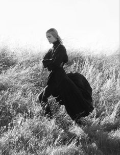 black and white photograph of woman in long dress running through tall grass with her back to the camera