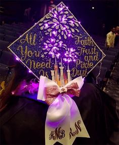 a woman wearing a graduation cap decorated with flowers and sparkles at the top, in front of an auditorium filled with people