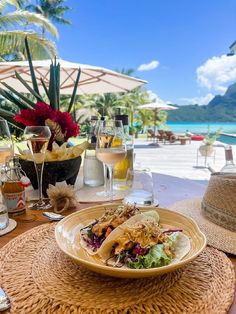 a plate of food and wine on a table with an ocean view in the background