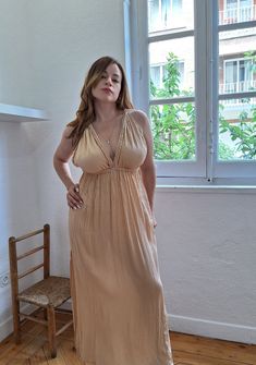 a woman standing in front of a window with her hands on her hips wearing a tan dress