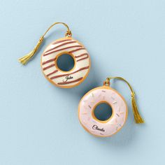 two donuts hanging from tassels on a blue background, one has a pink frosted donut with chocolate icing and the other has a tassel