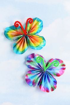 two colorful paper butterflies sitting next to each other on a white surface with blue sky in the background