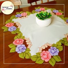 a table topped with a white vase filled with flowers on top of a wooden table