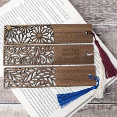 three laser cut bookmarks with tassels on top of an open book,