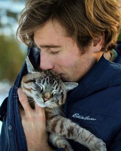 a man is holding a cat in his arms and kissing it's face with the other hand