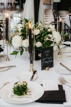 the table is set with white flowers and silverware for an elegant wedding reception in black and white