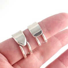 two pieces of metal sitting on top of a persons finger in front of a white background