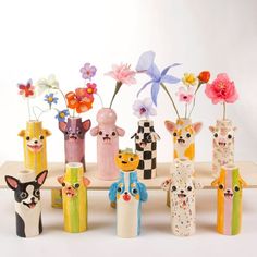 a group of small vases with flowers in them on a wooden shelf against a white background