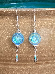 a pair of blue glass dangles hanging from silver earwires on a tan surface