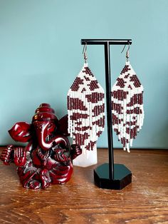 a pair of red and white beaded earrings sitting on top of a wooden table