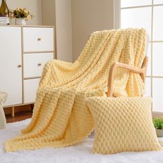 a yellow blanket sitting on top of a bed next to a white dresser and chair