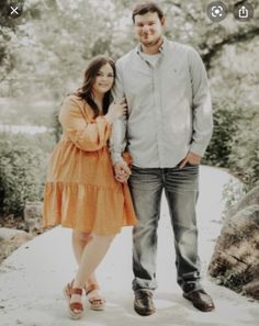 a man and woman standing next to each other on a path in front of trees