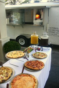 pizzas and drinks are on the table in front of an ice cream truck that is parked outside