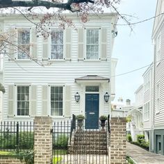 a white two story house with a blue door and black iron fence in front of it