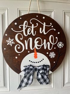 a wooden sign that says let it snow with a snowman in the center and a bow