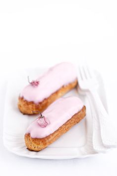 two donuts with pink icing sitting on a white plate next to a fork