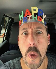 a man wearing a birthday hat in the back seat of a car with his tongue out