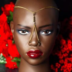 a mannequin's head is adorned with gold chains and red flowers in the background