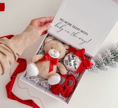 a person is holding a teddy bear in a gift box with red ribbon around it