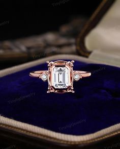 an emerald colored diamond ring sits in a velvet case on top of a blue velvet cushion