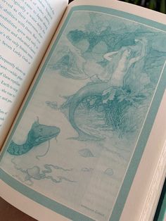 an open book with mermaids and sea creatures on the pages, in front of other books