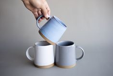 someone is pouring something into two mugs on top of the other one, which are both white and blue